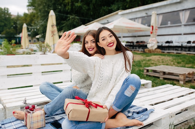 Two beautiful women sitting on a bench, holding gifts in their hands and looking