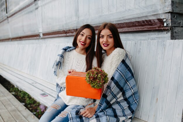 Two beautiful women sitting on a bench and holding in their hands gift