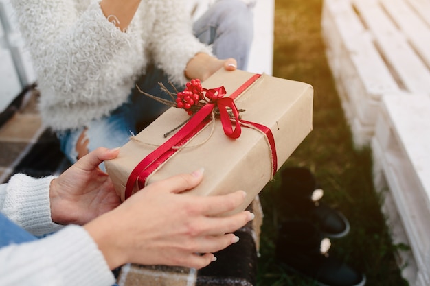 Two beautiful women sitting on a bench and holding in their hands gifts, close view