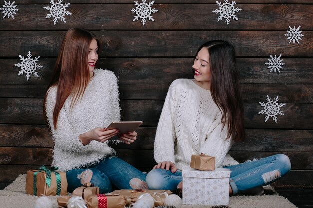 Two beautiful women sitting on the floor with a tablet, between gifts for Christmas