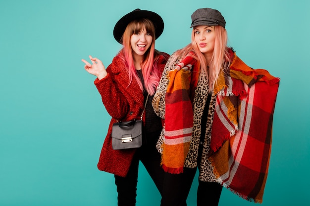 Beautiful women in faux fur coats and wool scarf posing on turquoise wall