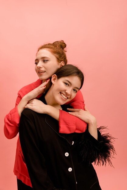 Two beautiful young caucasian woman in red and black shirts spend time together on pink background Leisure lifestyle concept