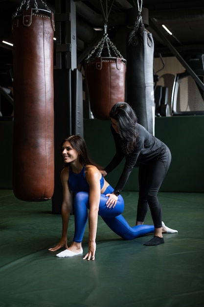 Две красивые молодые девушки делают фитнес в тренажерном зале. Растяжение мышц спины и ног.