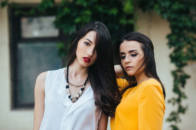 Two beautiful young girls in dresses posing in front of house