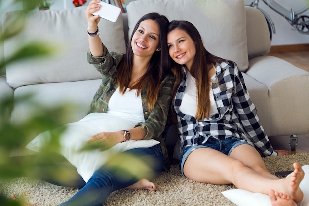 Due belle giovani donne utilizzando il telefono cellulare a casa.