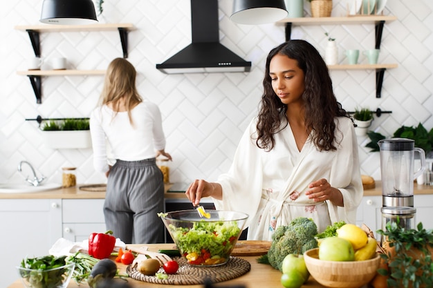 Two beautiful young women on the white modern kitchen are making healthy breakfast