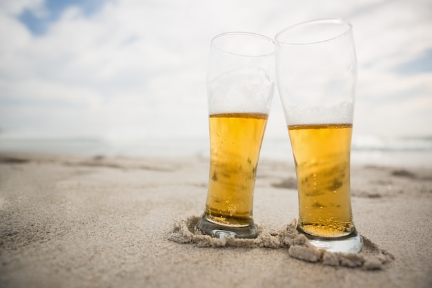 Two beer glasses kept on sand