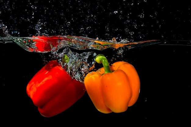 Two bell pepper falling into the water on black background