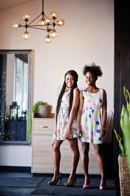 여름 드레스 하이힐에서 두 흑인 아프리카 여자 친구는 현대 집에서 포즈