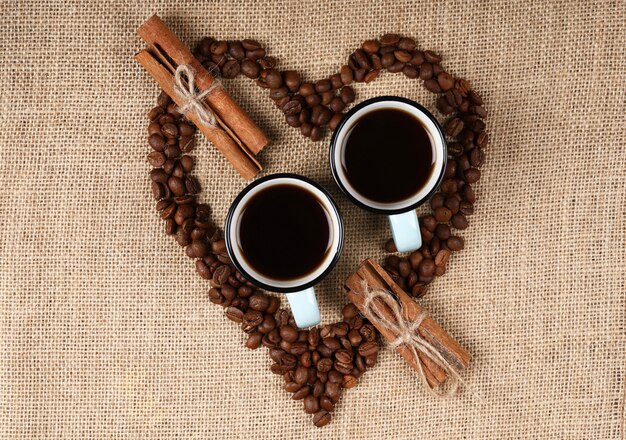 Две синие чашки кофе внутри кофейных зерен в форме сердца на мешковину