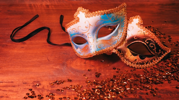 Two blue and golden carnival mask with glittering sequins on wooden desk