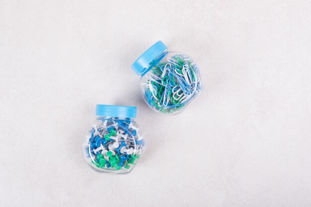 Two blue jars full of colorful pins and paper clips on beige background. High quality photo
