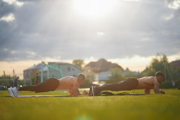 Two bodybuilders standing in plank position outdoors