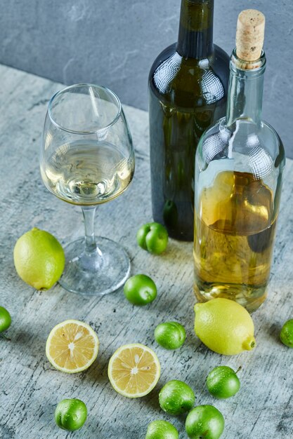 Two bottles and glass of wine on marble table with lemons and cherry plums