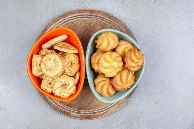Two bowls of biscuit and cookie chips on wooden board on marble background. High quality photo