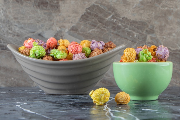 Two bowls of colorful tasty popcorns on marble surface. 