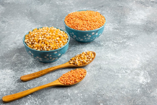 Free photo two bowls of corn kernels and red lentil on marble surface.