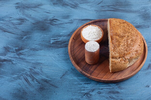 Two bowls of flour and sliced bread on a plate, on the blue.