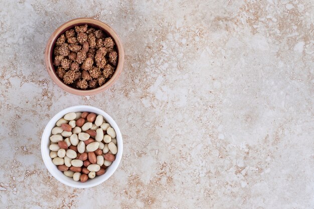 Two bowls of healthy peeled peanuts placed on a stone background .