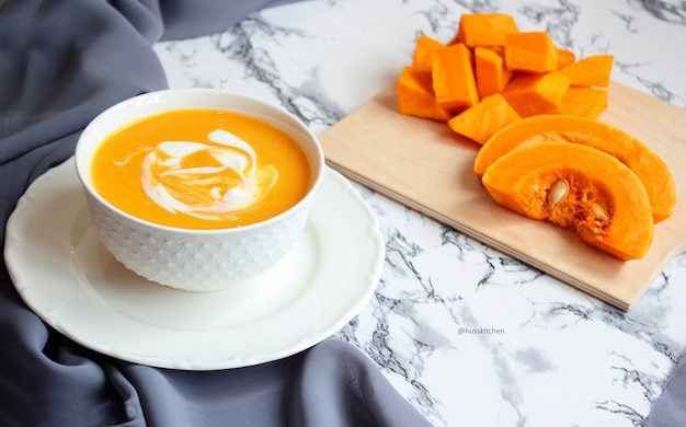 Two bowls of pumpkin soup with gray fabric and slices of butternut squash, top view, vegetarian food