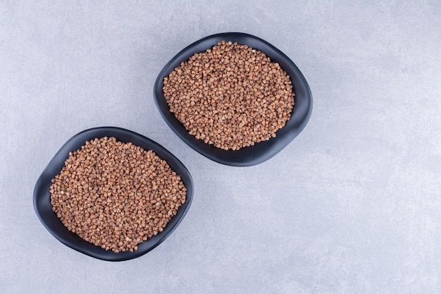 Two bowls of raw buckwheat on marble surface