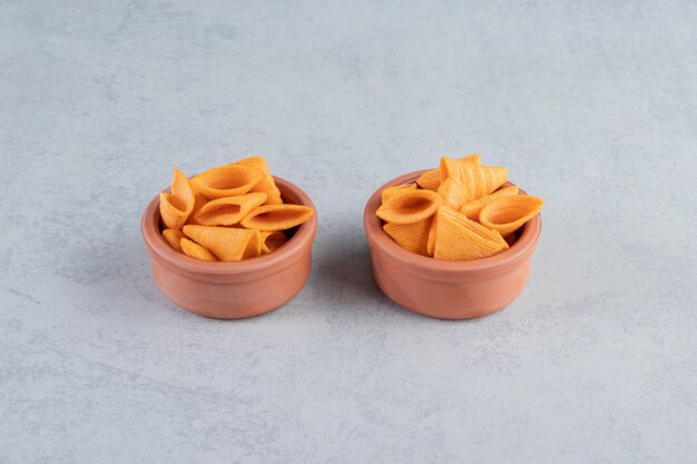 Two bowls of triangle shaped crispy chips on stone background.