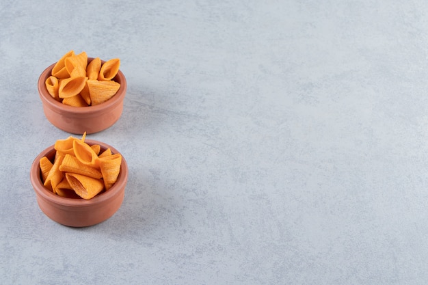 Two bowls of triangle shaped crispy chips on stone background