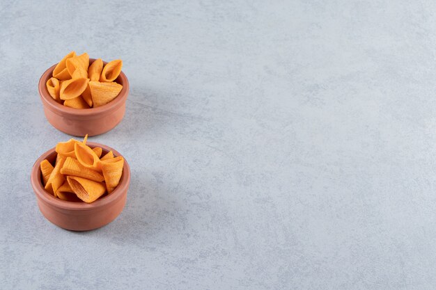 Two bowls of triangle shaped crispy chips on stone background.