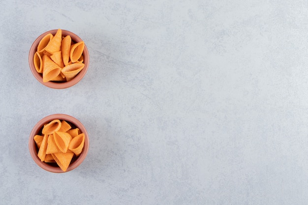 Two bowls of triangle shaped crispy chips on stone.