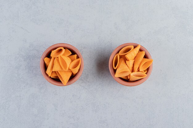 Two bowls of triangle shaped crispy chips on stone.