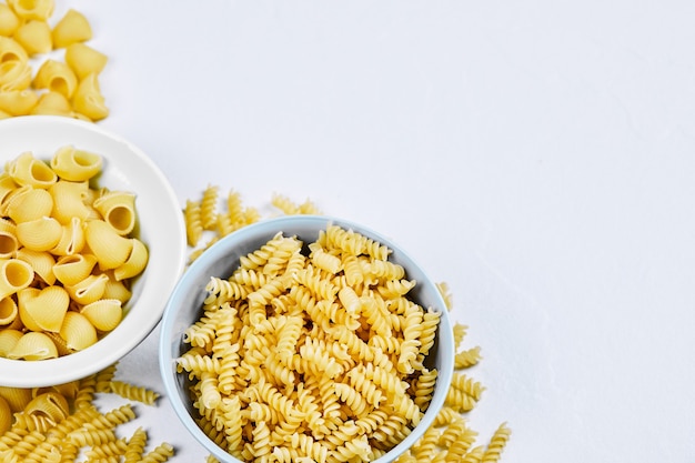 Two bowls of uncooked pastas on white background