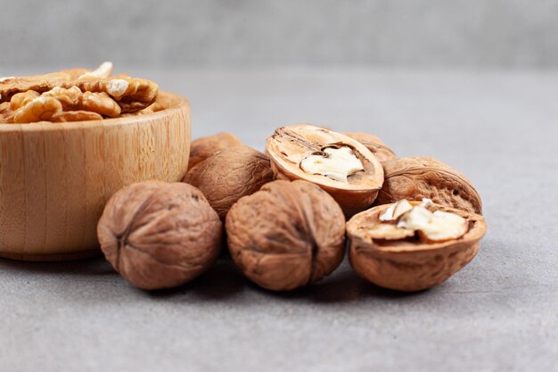 Two bowls of whole and cracked walnuts on marble surface.