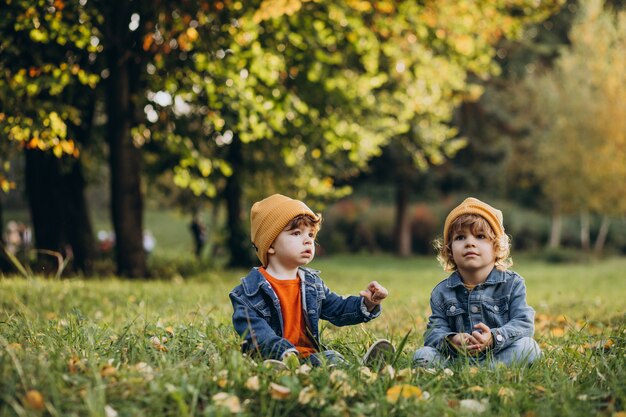 Two boys brothers sitting on grass under the tree