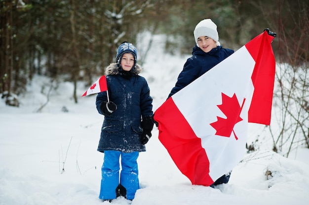 冬の風景にカナダの旗を保持している2人の男の子。 Premium写真