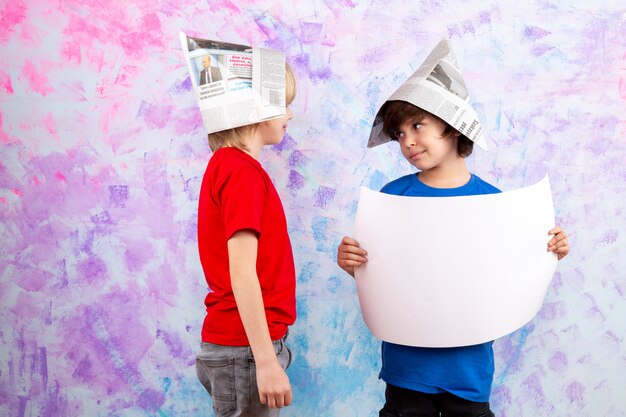 two boys in red t-shirt and blue t-shirt with wallpaper hats on colorful wall