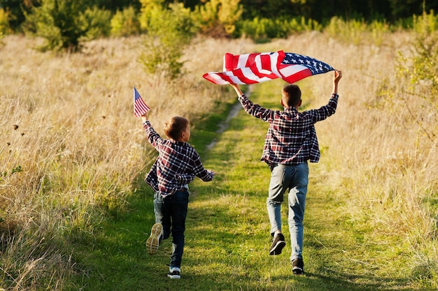 アメリカの国旗を掲げて走る二人の兄弟アメリカの休日国の子供であることを誇りに思う