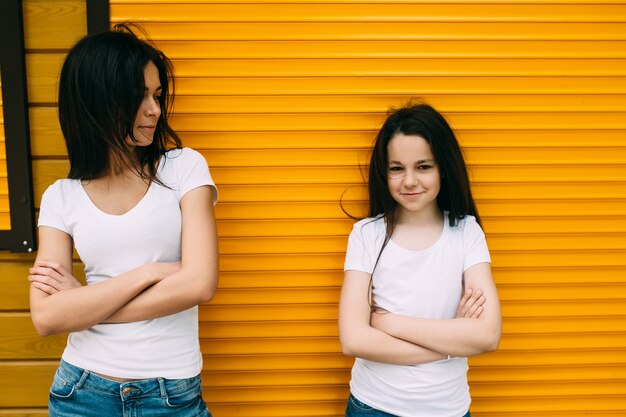 Two brunette girls standing against orange wall