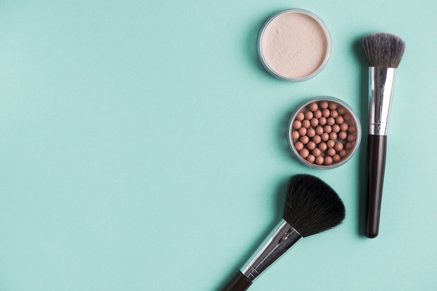 Two brush with compact and bronzed pearls over green background