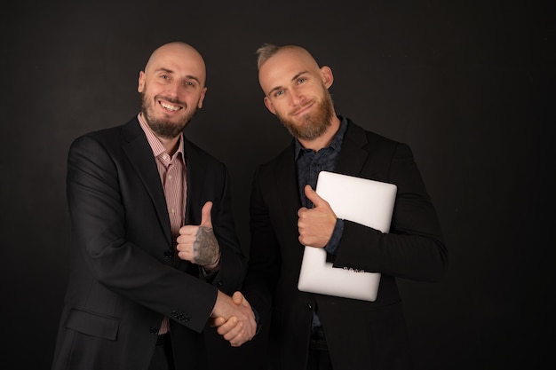 Two brutal bearded men in suits on black rejoice, businessmen with a laptop made a deal