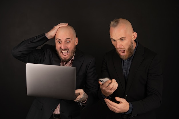 Two brutal bearded men in suits on black scream with happiness, rejoice, the cryptocurrency has grown, businessmen with a laptop