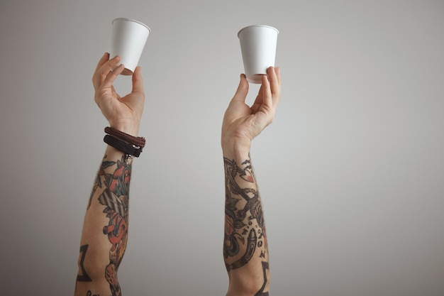 Two brutal tattooed men hands hold blank paper take away cardboard glass in the air. presentation isolated on white.