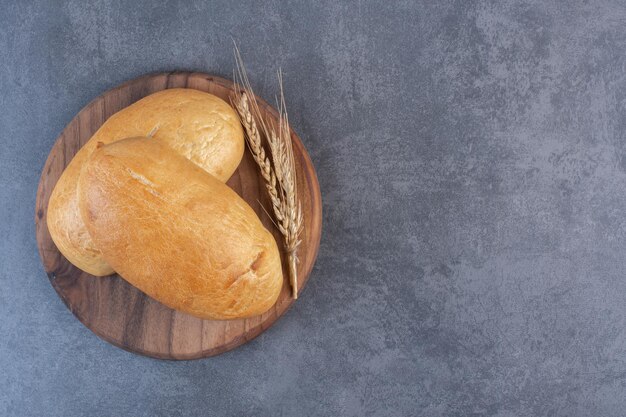 Two buns and a single wheat stalk on a wooden board on marble background. High quality photo