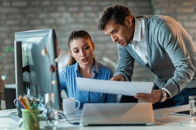 Two business colleagues talking while working on a new project and examining blueprints in the office