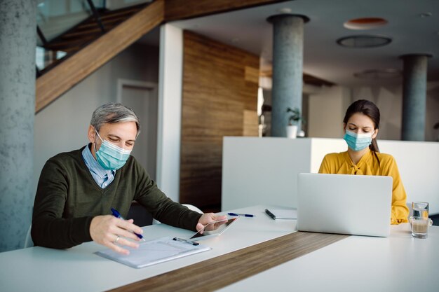 Two business coworkers wearing face masks while working together in the office