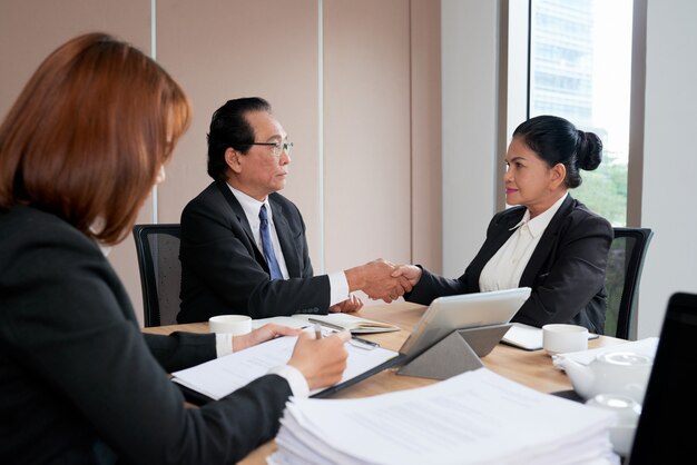 Two business executives handshaking to close the deal while the secretary protocoling the minutes of the meeting