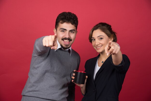 Two business partners pointing at front on red wall