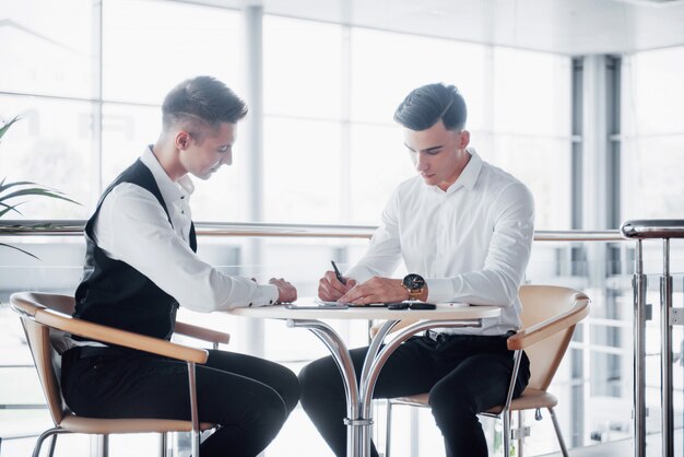 Two business people sign documents in a large, spacious office