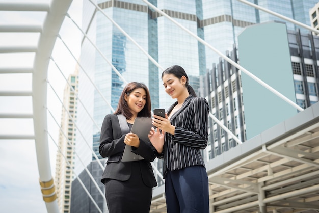 Две деловая женщина, стоя с использованием смартфона и обсуждения в передней части офиса. Концепция деловой работы.