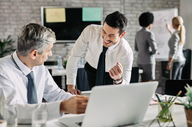 Two businessmen communicating while using computer in the office Focus is on young happy businessman