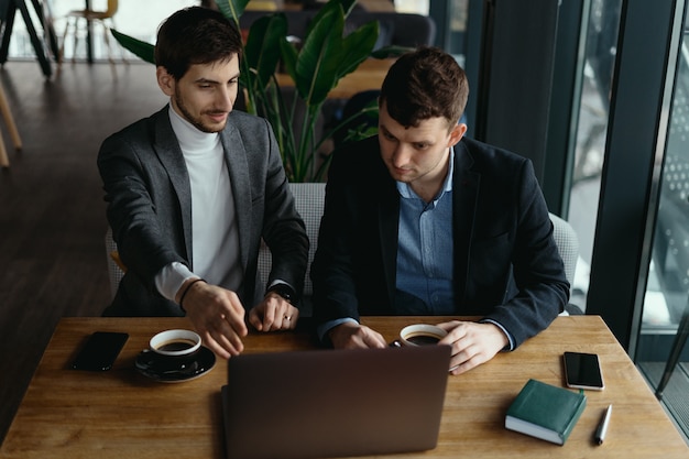 Two businessmen pointing laptop screen while discussing